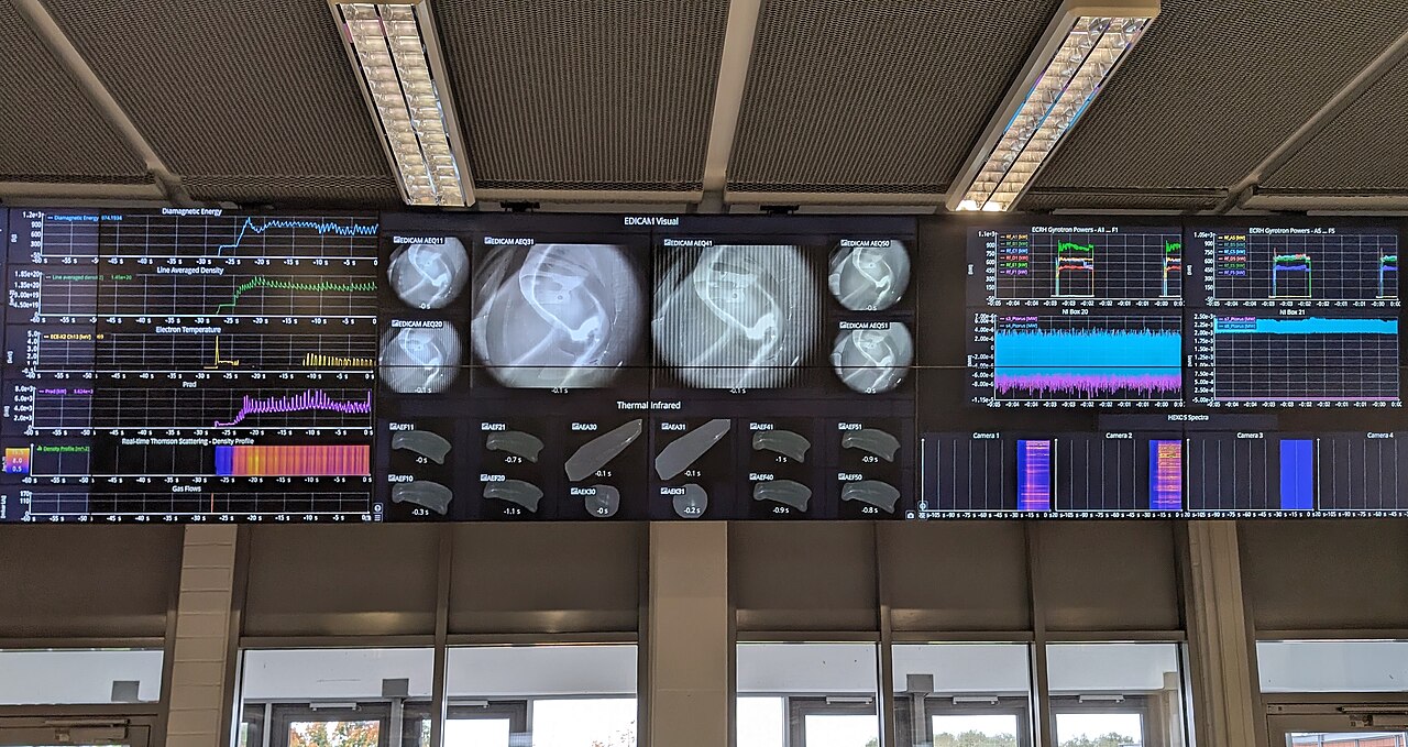 Control room consoles with status dashboards and monitoring screens in a dim operations center